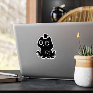Laptop with a black sticker of a cute creature on a desk with a plant and pen.